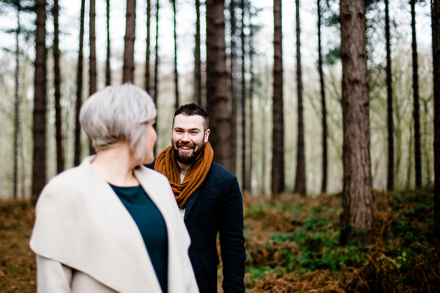 man and woman looking at each other stood among pine trees