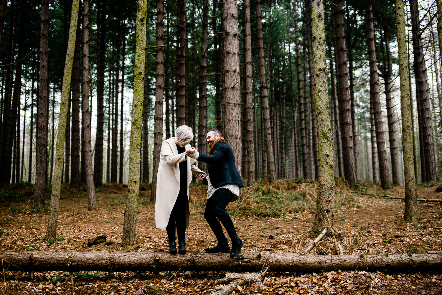 A couple having fun balancing on a log in a Yorkshire pine tree woodland
