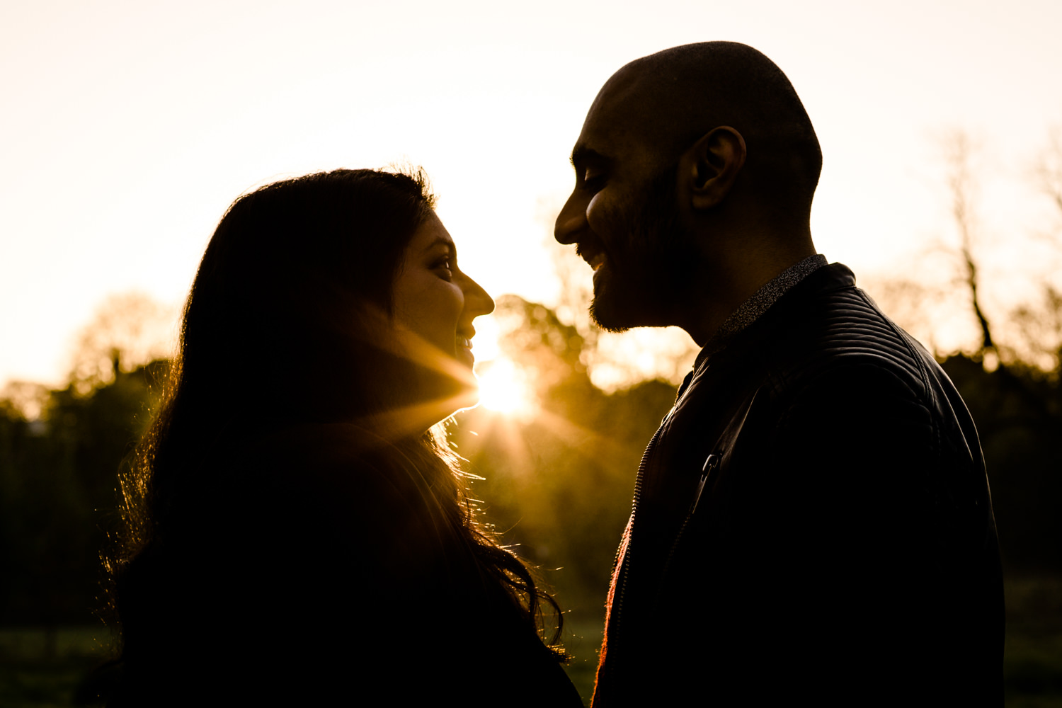 Star burst of sun light at sunrise in between a silhouette of a smiling couple, in Fetcher Moss Park, Manchester.
