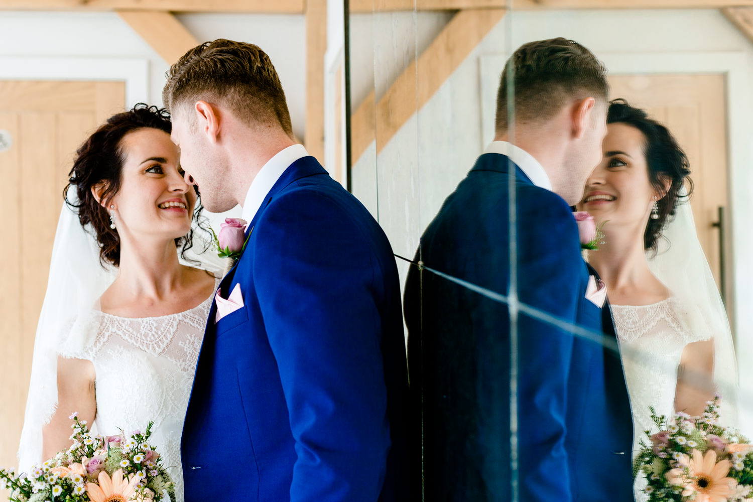 A wedding couple close together with their refection in a mirror.