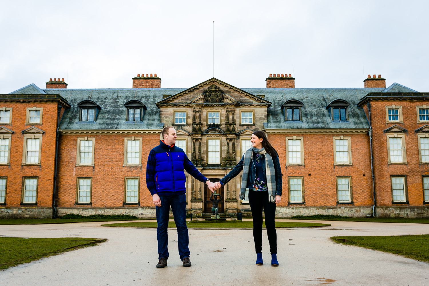 An engaged couple holding hands in front of Dunham Massey manor house. 