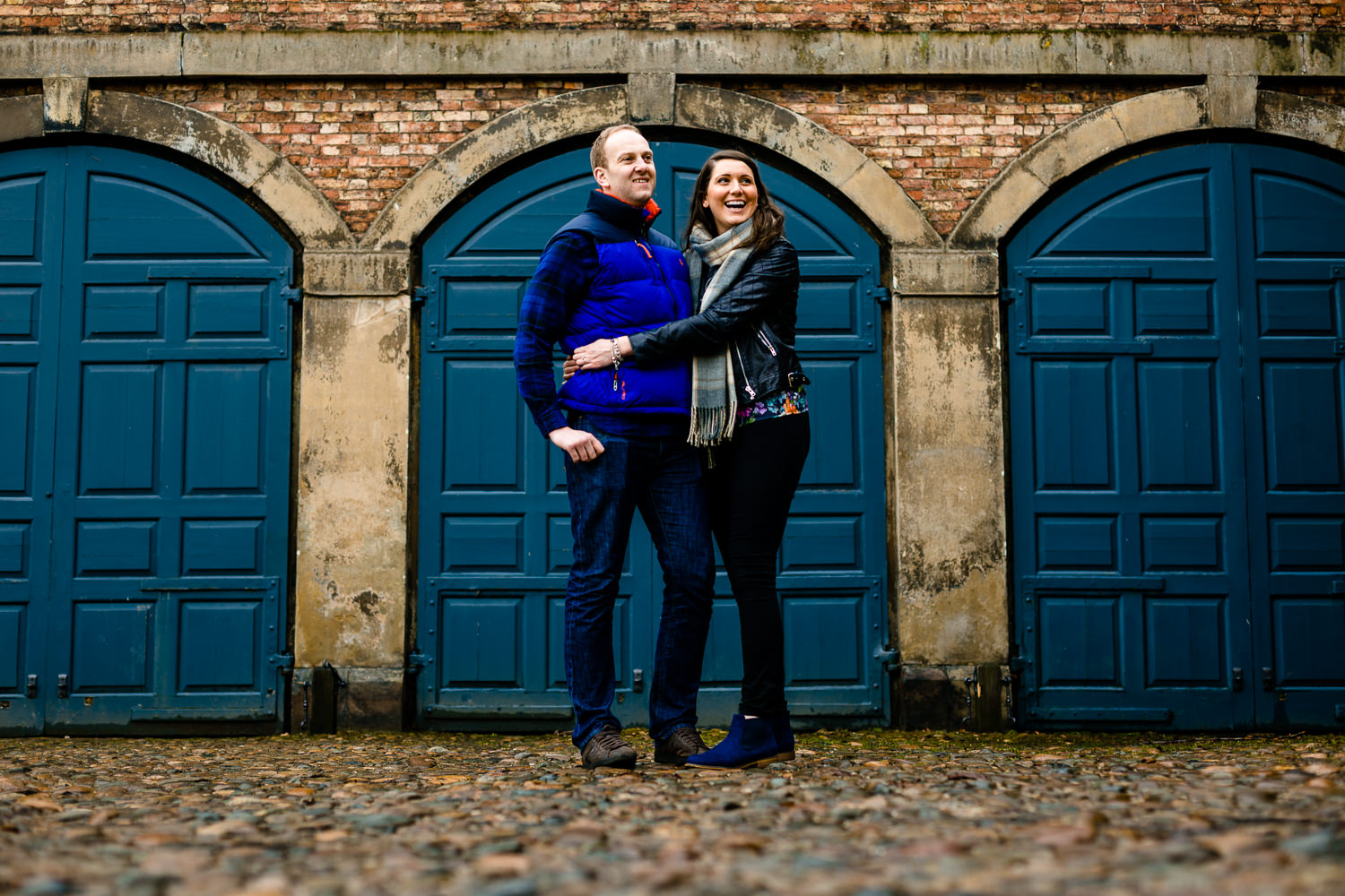 Dunham Massey pre wedding shoot, a couple laughing and cuddling in front of the blue coach house doors. 
