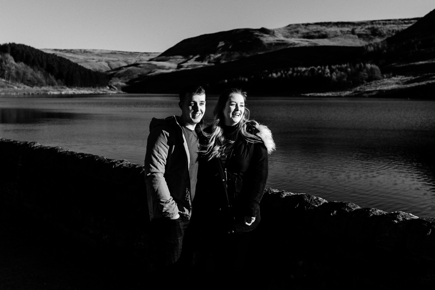 A couple laughing on their pre wedding shoot next to a reservoir. 