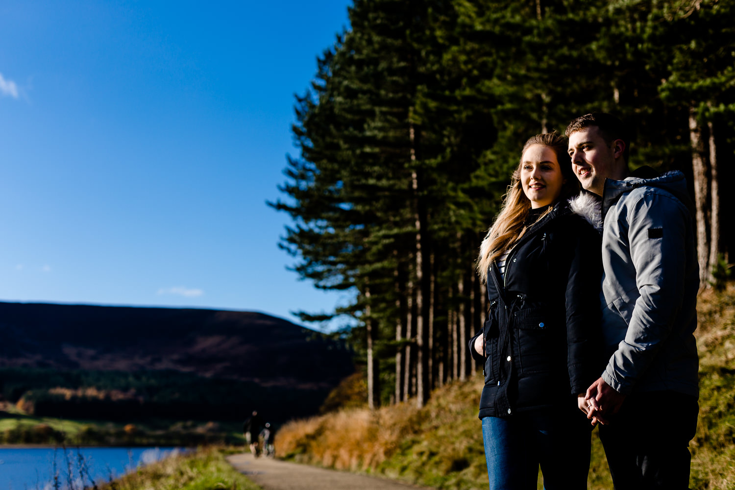 A couple stood alongside a reservoir and pine trees in Manchester.