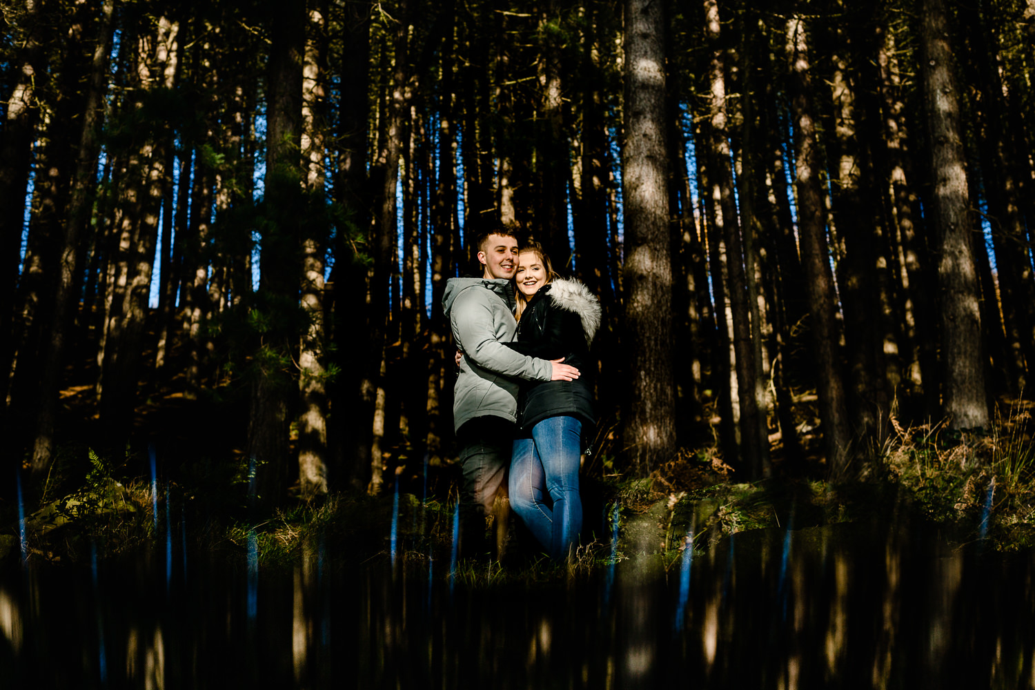 Manchester wedding photographers capture a couple in beautiful dappled light among pine trees at Dovestone reservoir on their pre wedding shoot. 