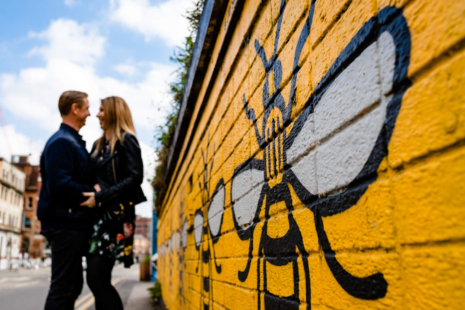 A couple stood next to the Manchester Bee wall art in the Northern Quarter on their pre wedding shoot. 