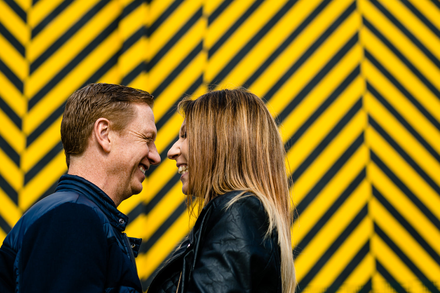 A couple laughing in front of Hacienda inspired street art in Manchester.