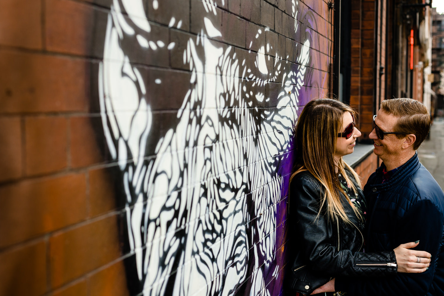 A couple cuddle in front of Norther Quarter street art on their pre wedding shoot. 