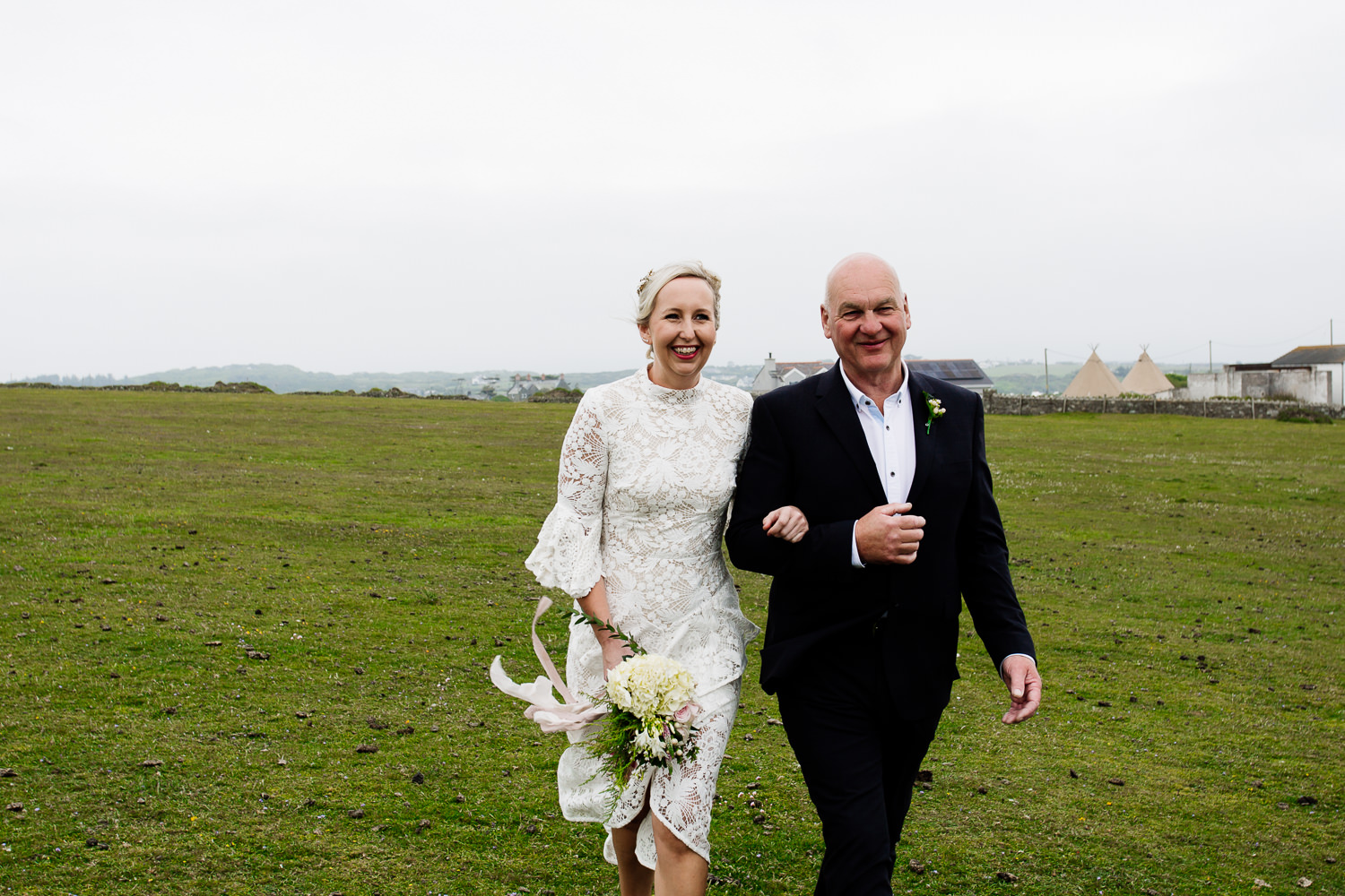 Bride with her father walking towards her groom on the headland in Anglesey