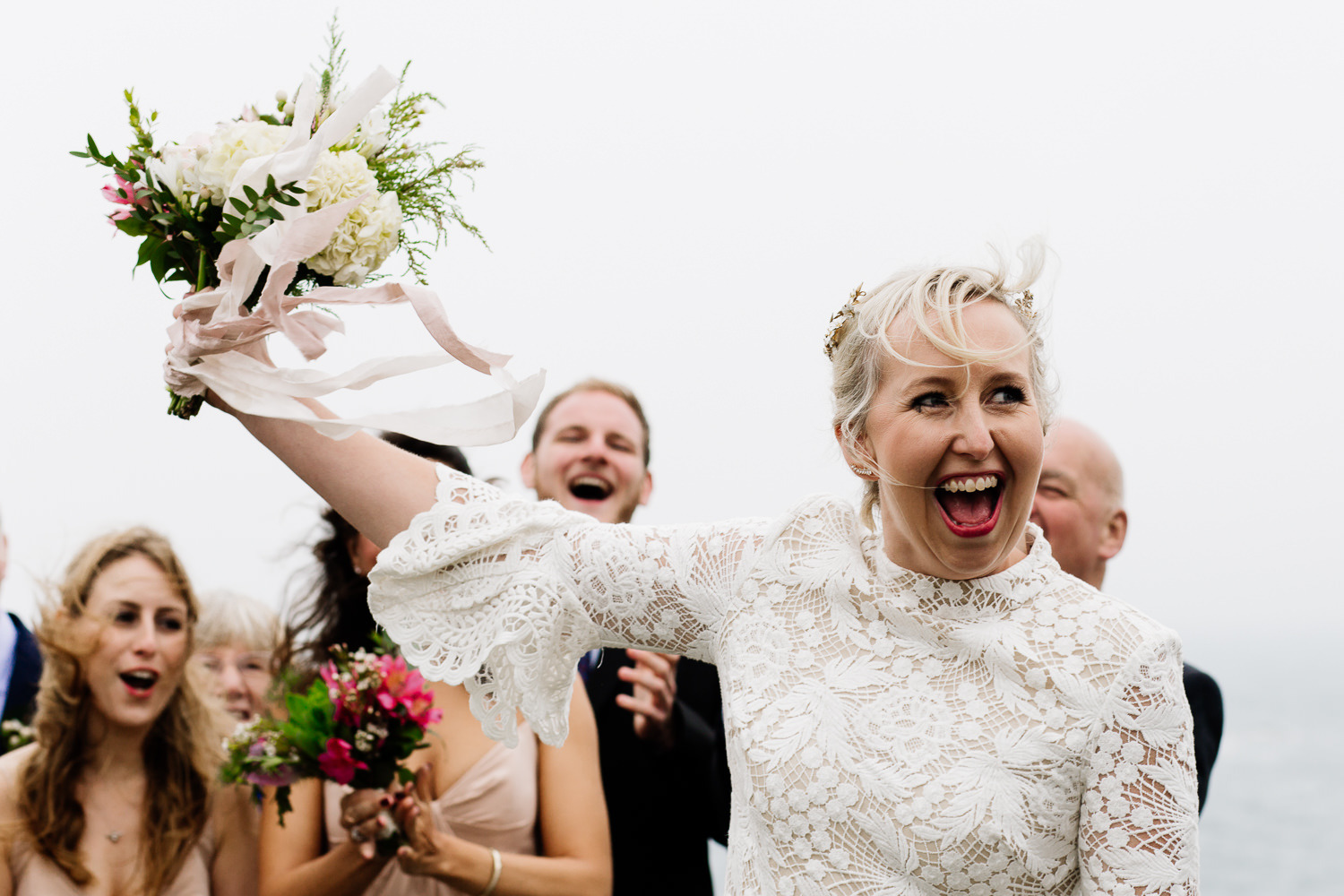 A bride celebrating getting married with her bouquet in the air a an outdoor ceremony in Anglesey, Wales.