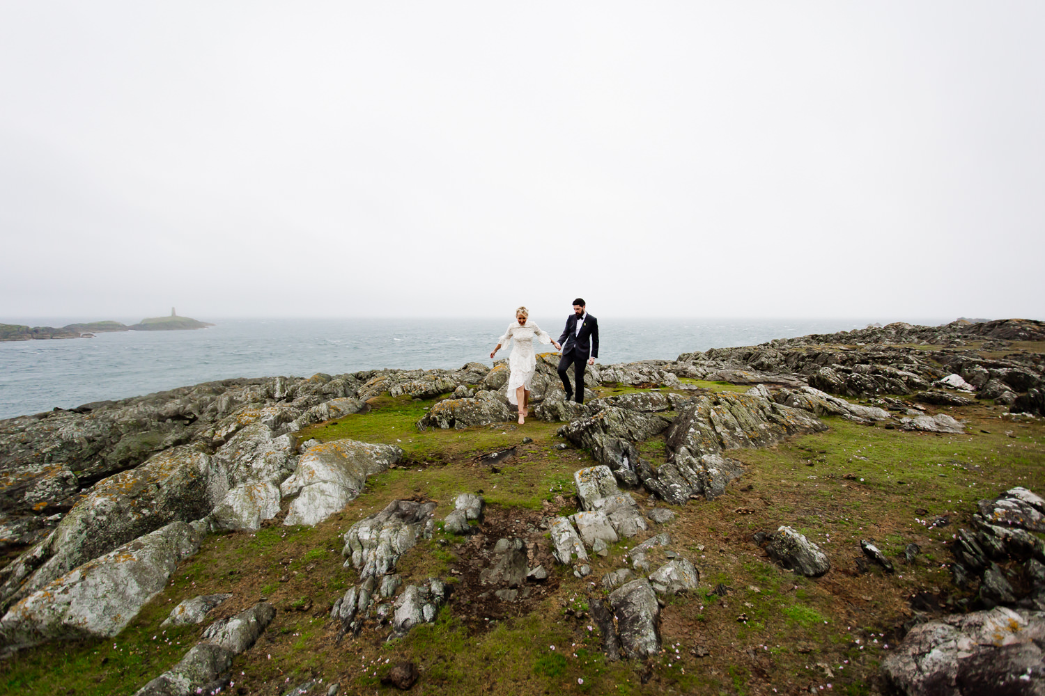 Bride and groom walking along the cliffs together at their tipi wedding in Anglesey. 