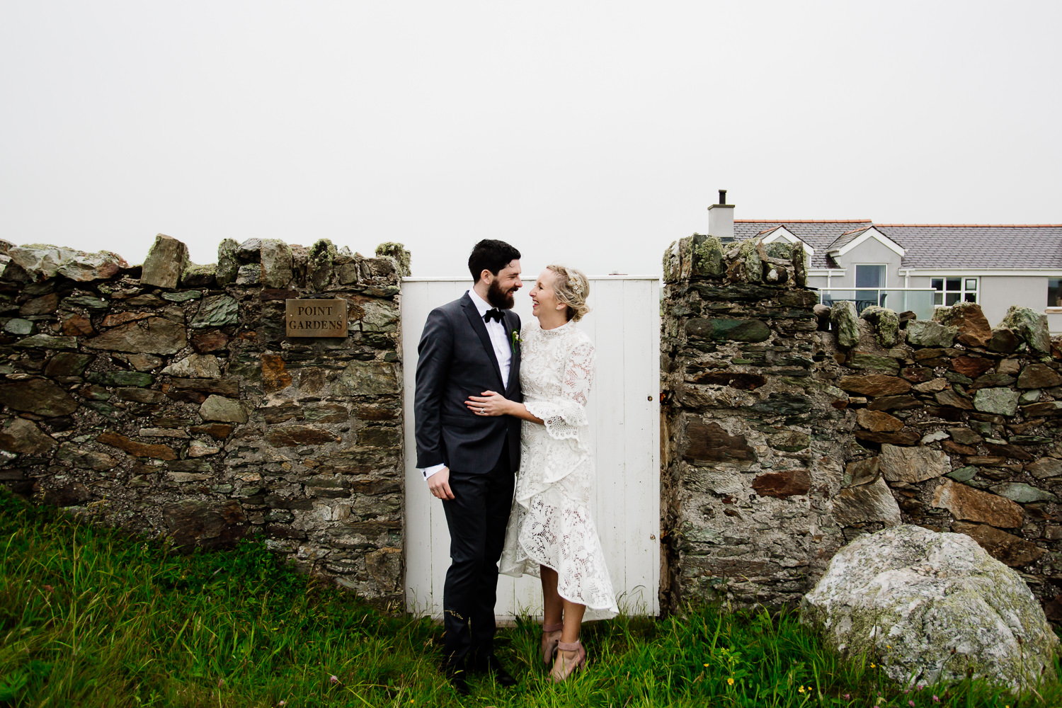 Relaxed, festival, tipi wedding in Wales, the bride and groom stood in front of a garden gate.