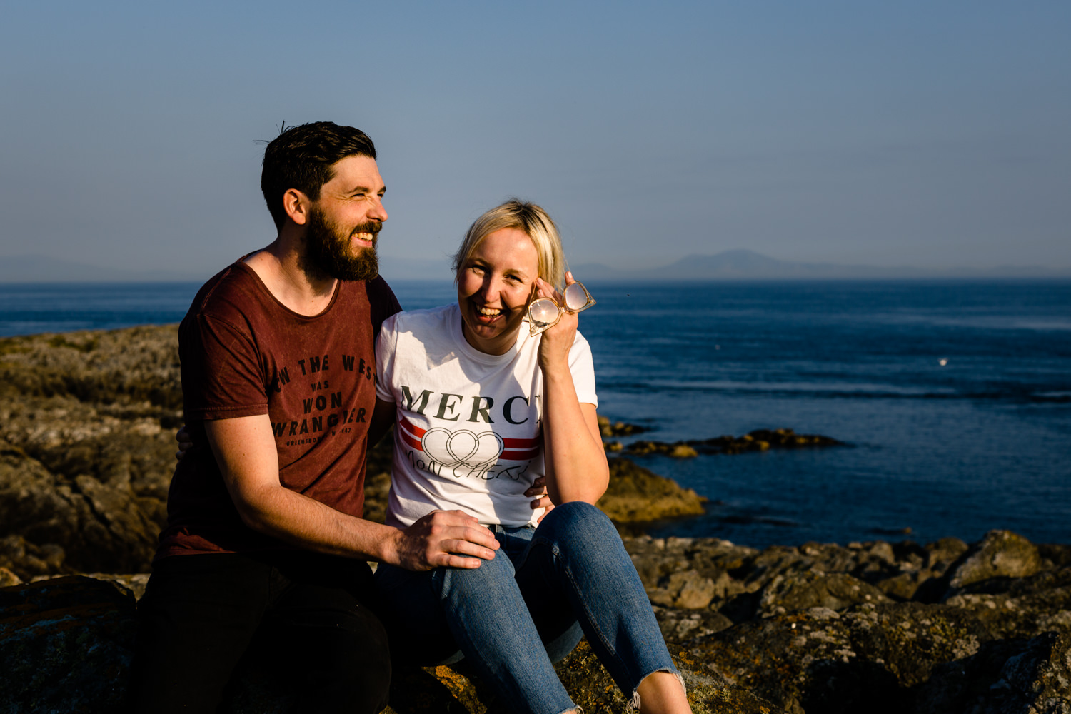 Katie & Sean sat on the rocks on the Anglesey headland, laughing together. 
