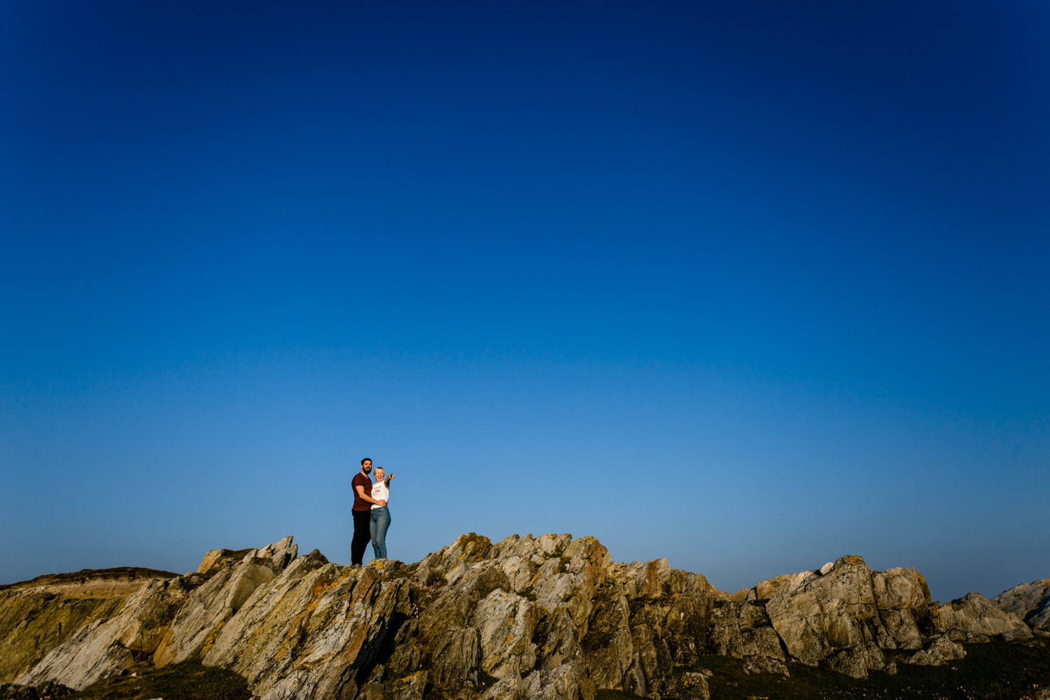 An engaged couple pointing out to sea whilst stood on the Anglesey headland on a pre wedding shoot. 