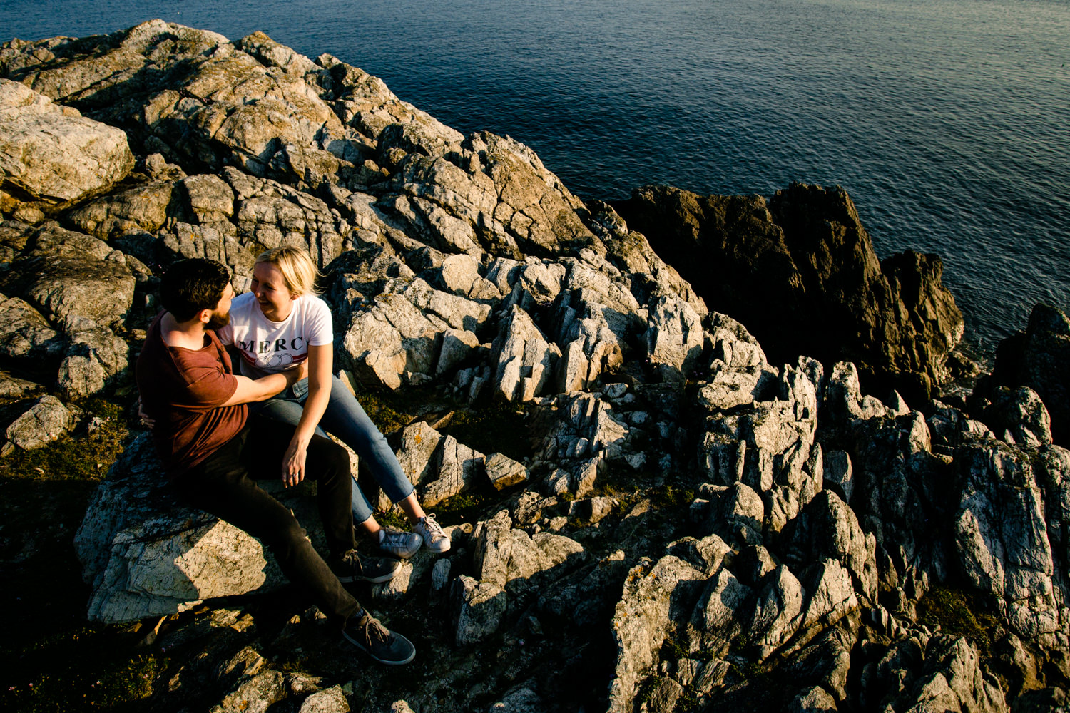 A view down the cliff rocks in Anglesey, of a couple sat cuddling.