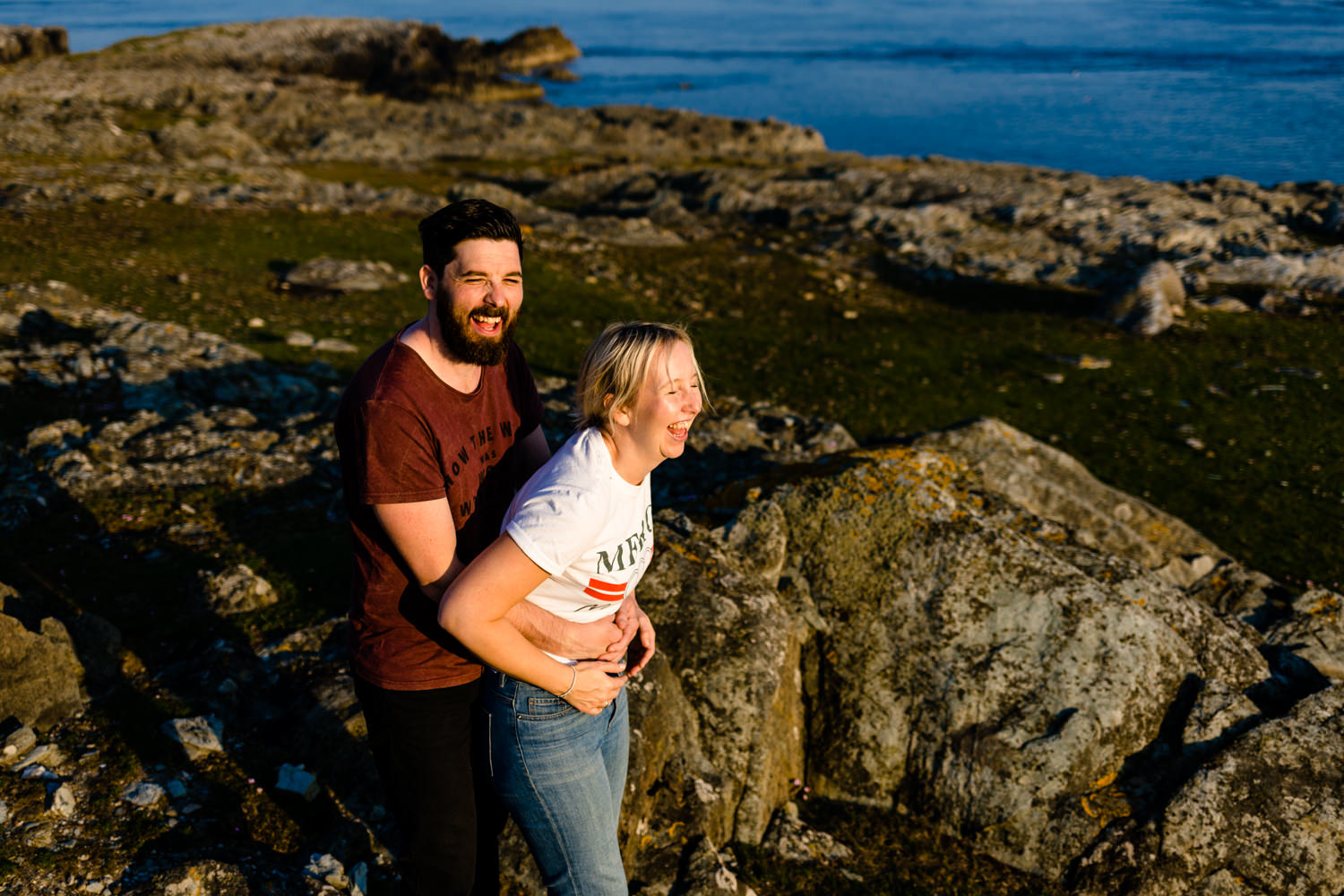 A couple laugh together lit by the golden hour sun on the headland in Anglesey.