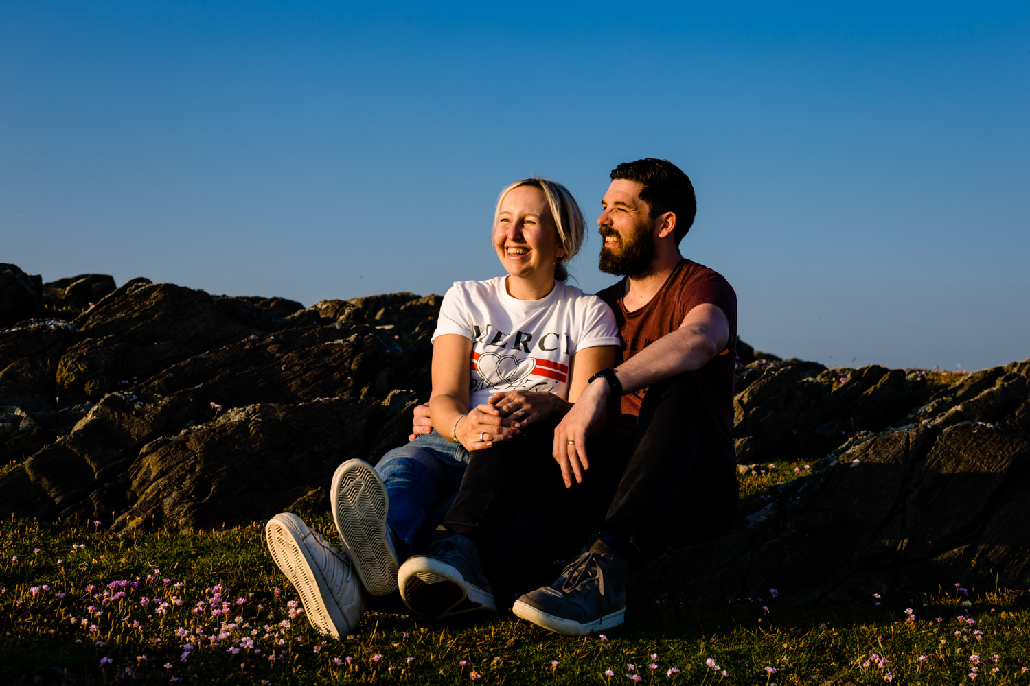 A couple sat watching the sunset on their pre wedding shoot, by Anglesey wedding photographers Zoe & Tom 