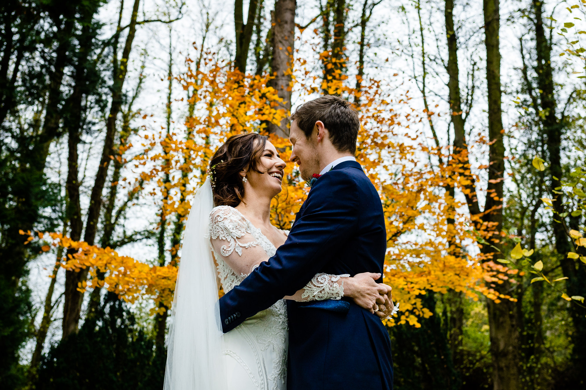 Bride and groom with a colourful autumn backdrop in the forest grounds of Tyn Dwr Hall, by wedding photographers Zoe & Tom