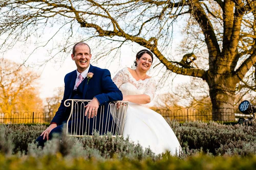 A laughing wedding couple sat in the Iscoyd Park garden, wedding photography by Zoe and Tom of About Today Photography