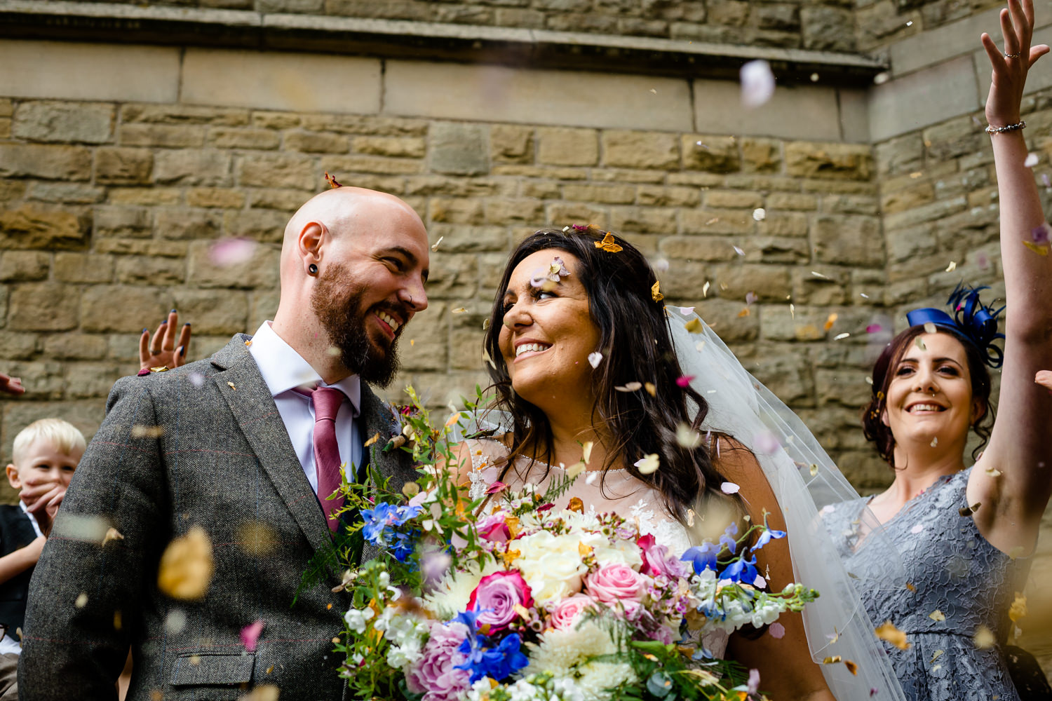 A bride and groom smile at each other with confetti