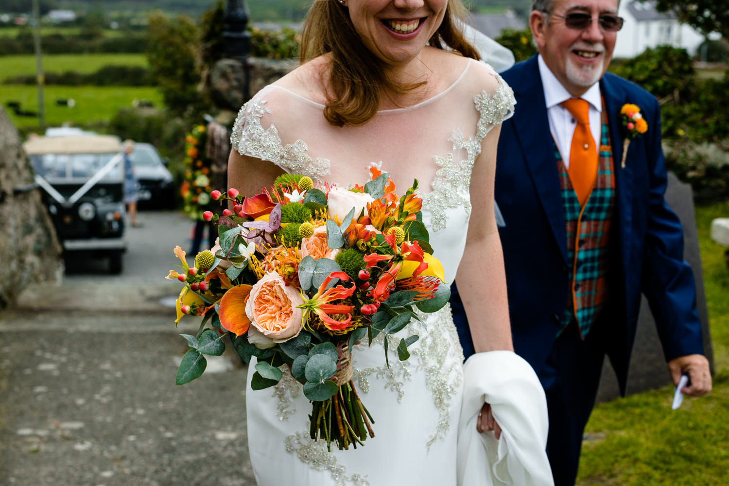 A bride carrying a bright bouquet on the way to church, Colourful Anglesey wedding photos
