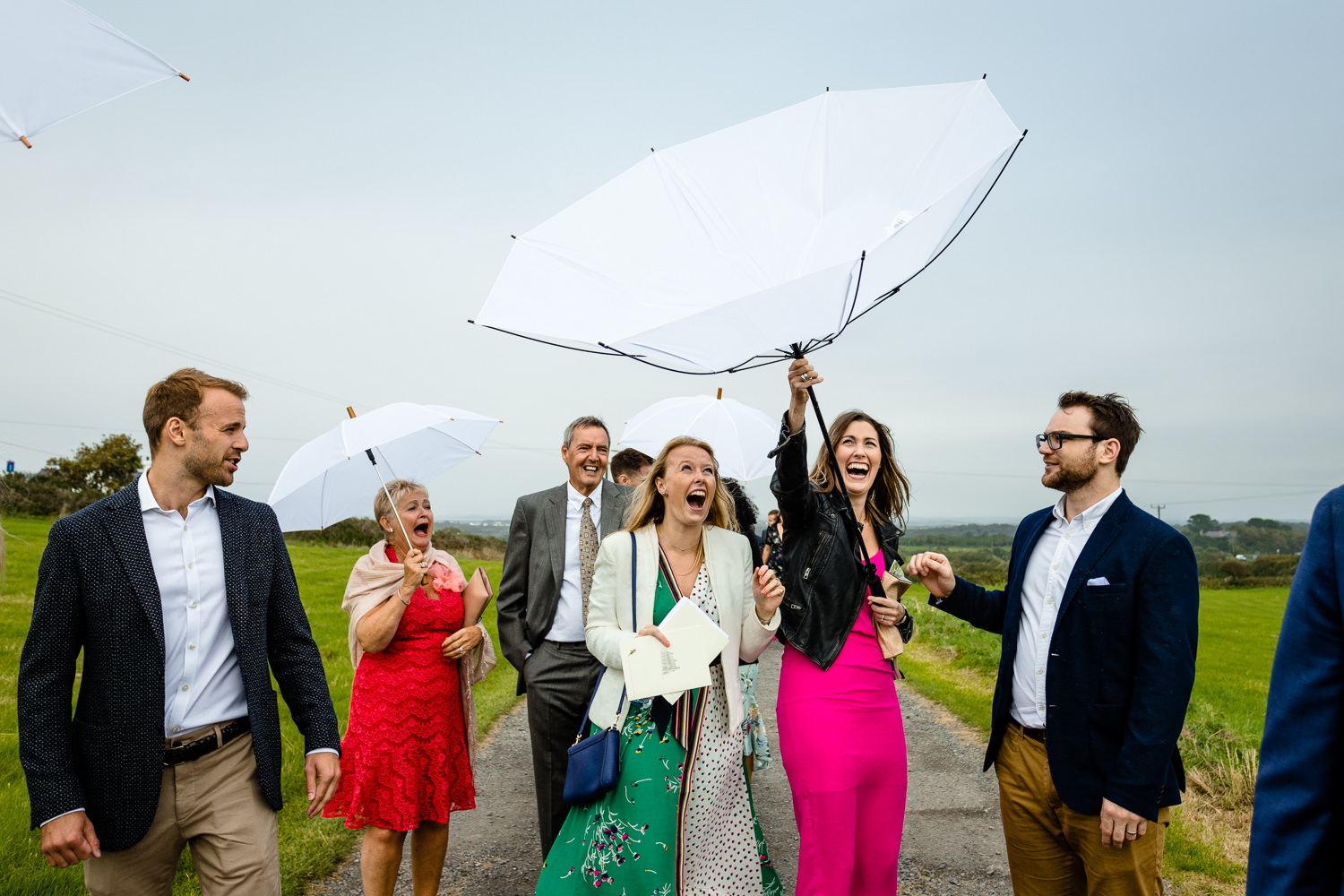 A wedding guest laughs as her umbrella turns inside out in the wind relaxed Anglesey wedding photography