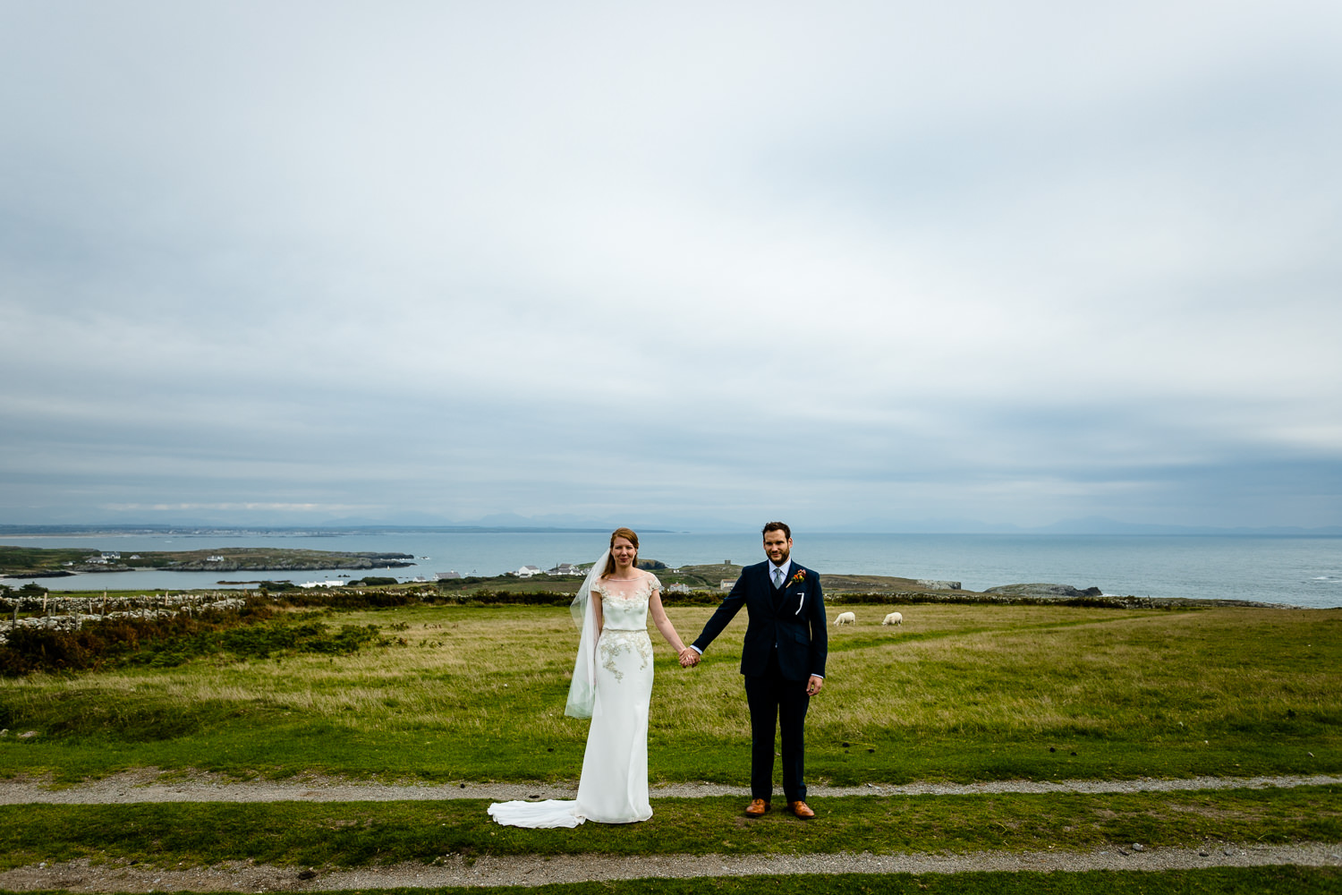 A bride and groom stood on the Rhoscolyn headland by an Anglesey wedding photographer