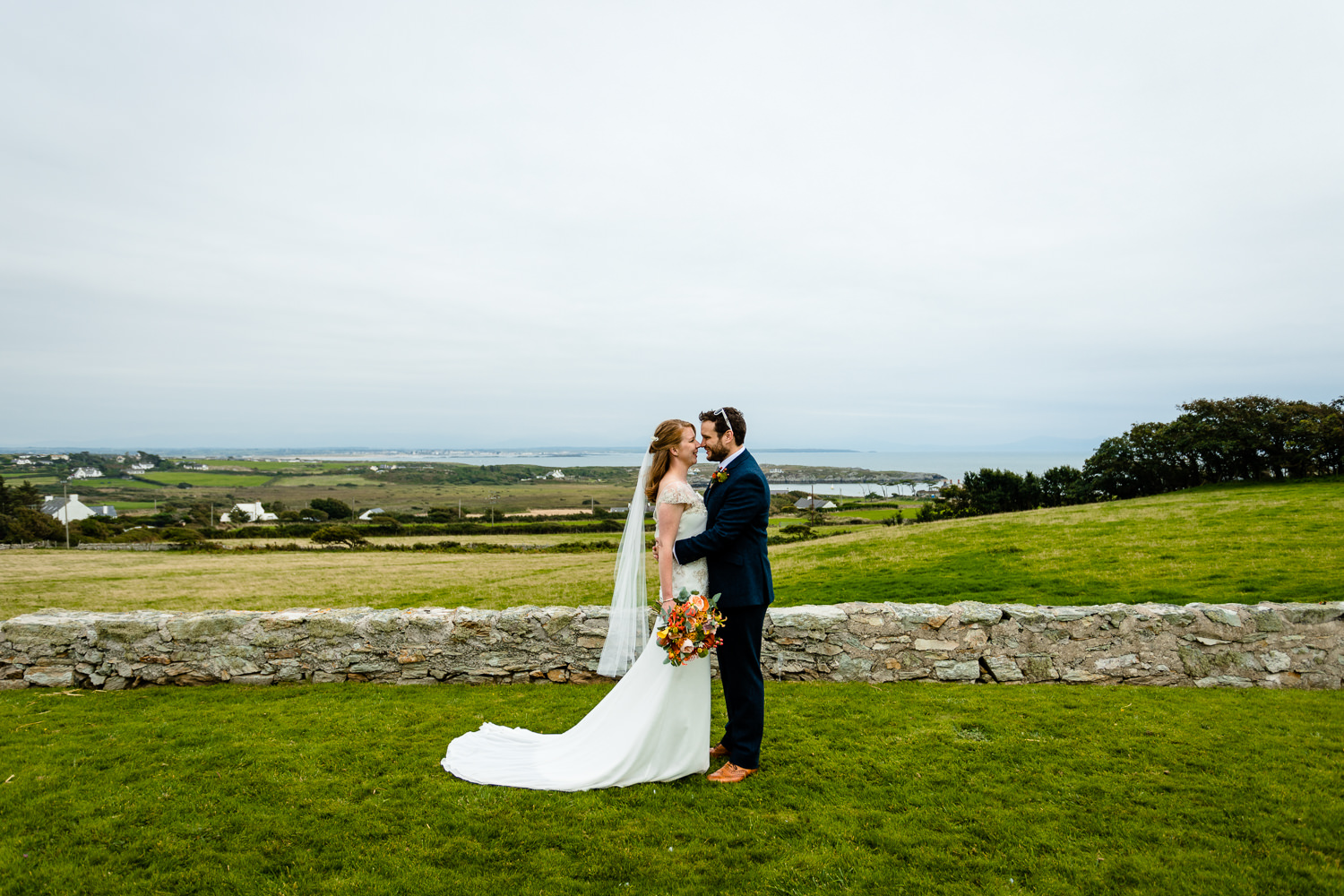 A bride and groom facing each other in front of the bay at Rhoscolyn, Colourful Anglesey wedding photographers