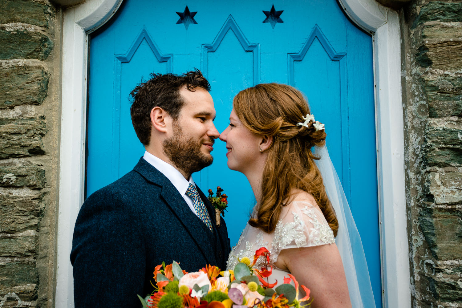 Anglesey wedding photographs of a bride and groom in front of a bright blue doorway in Rhoscolyn