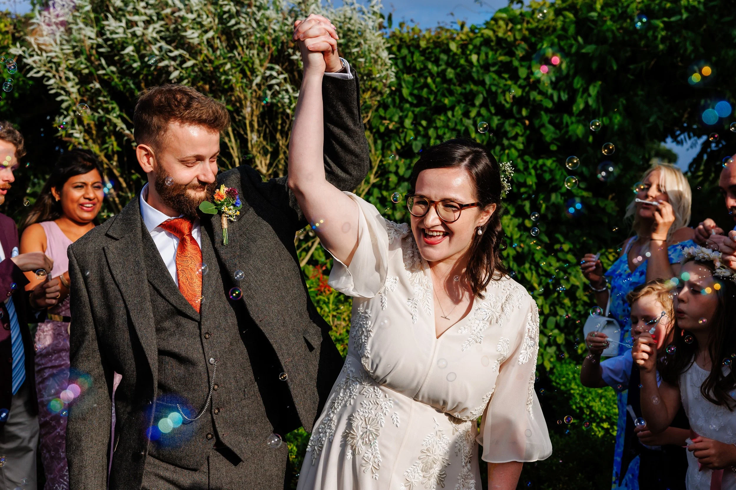 Hannah and Ron on their wedding day celebrating with arms in the arm as they walk through a bubble tunnel