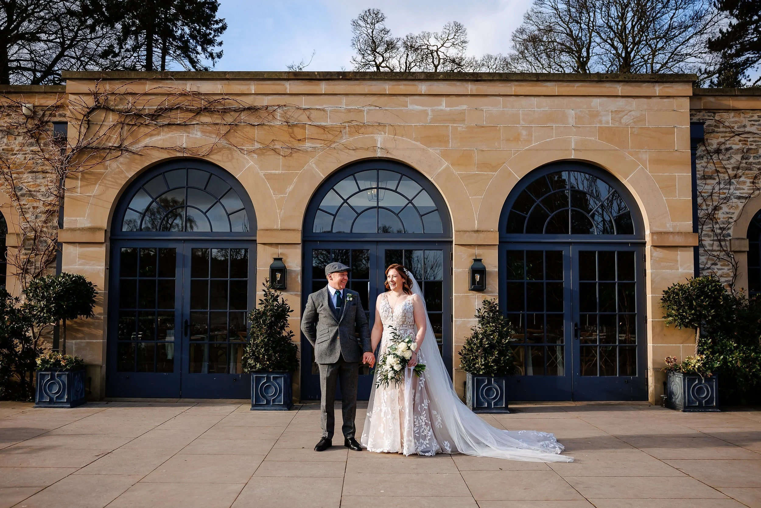 Bride and groom on their wedding day, stood in front of the arched windows of the Fig House at Middleton Lodge Estate in Yorkshire