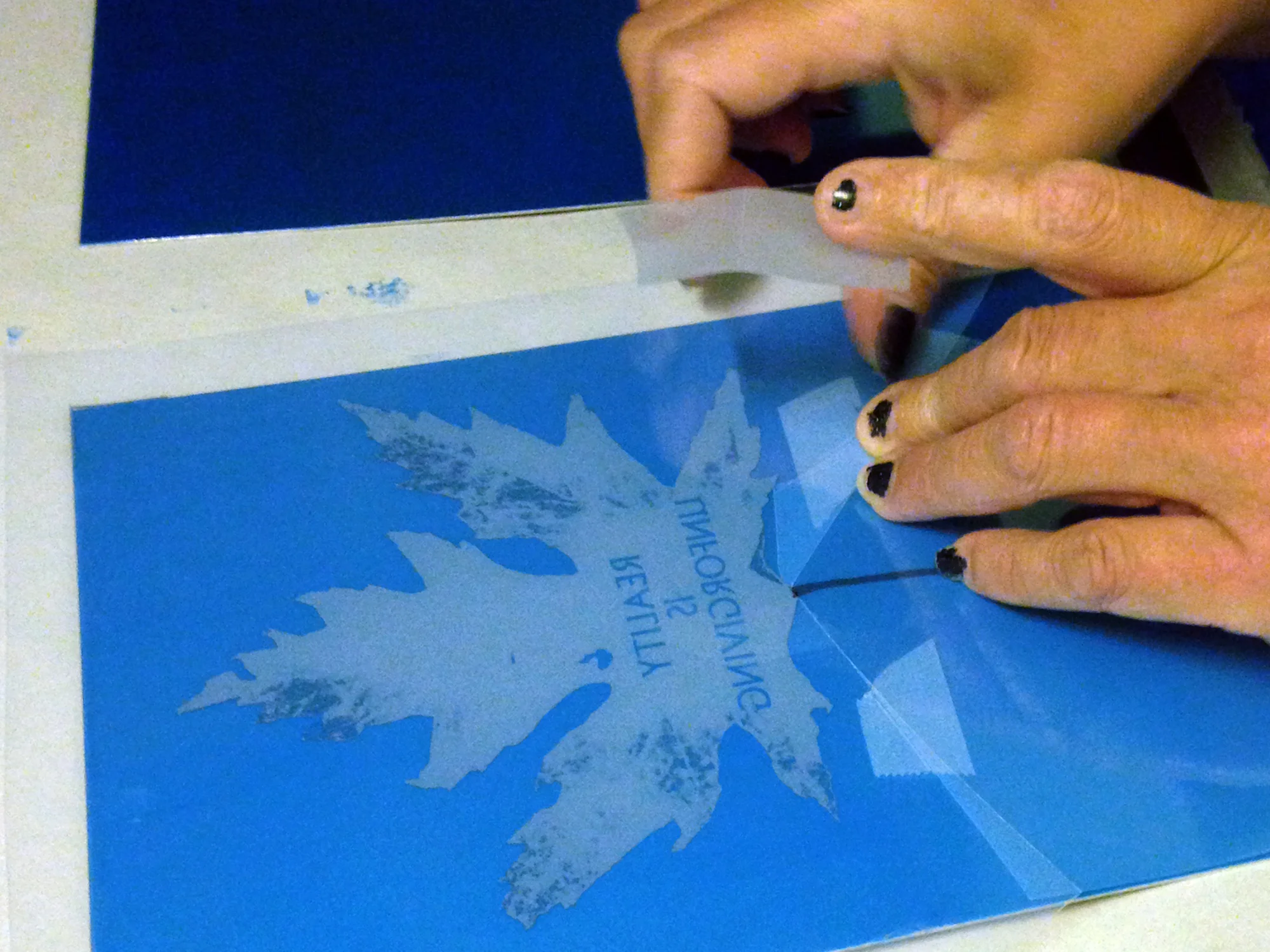 Etching plate is coated in light sensitive emulsion. The film is placed, and exposed to UV light as a negative image