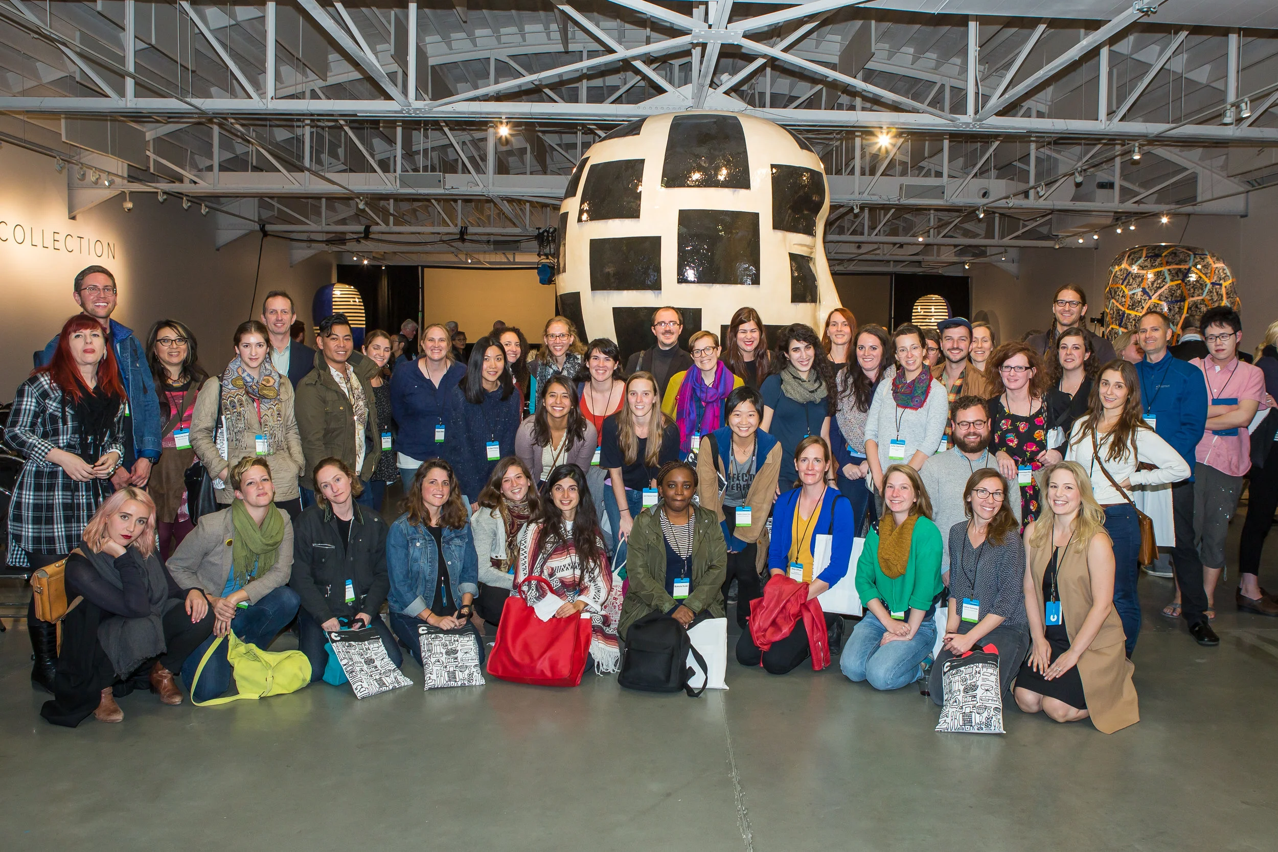 The 2016 American Craft Council Present Tense Conference Scholarship Award Recipients at the industrial-chic venue KANEKO , with Jun Kaneko 's ceramic heads in the background. Photo by Ben Semisch . 