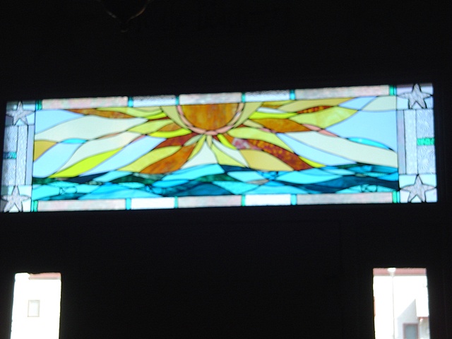  Sunrise Over Brigantine (installed)  Stained Glass  This is a view of the transom window after installation. The rich turquoise and warm golden yellows provide an inviting accent to the entryway of this private residence.  This piece is now held in 