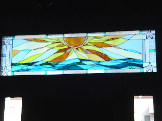 Sunrise Over Brigantine (installed) Stained Glass This is a view of the transom window after installation. The rich turquoise and warm golden yellows provide an inviting accent to the entryway of this private residence. This piece is now held in the Schimek Collection. Designing and fabrication typically are all done in our studio located on Long Beach Island, NJ. Custom work is one of our specialties, evidenced by our many happy repeat clients. We have a team of carpenters working with us for all your installation needs as well.