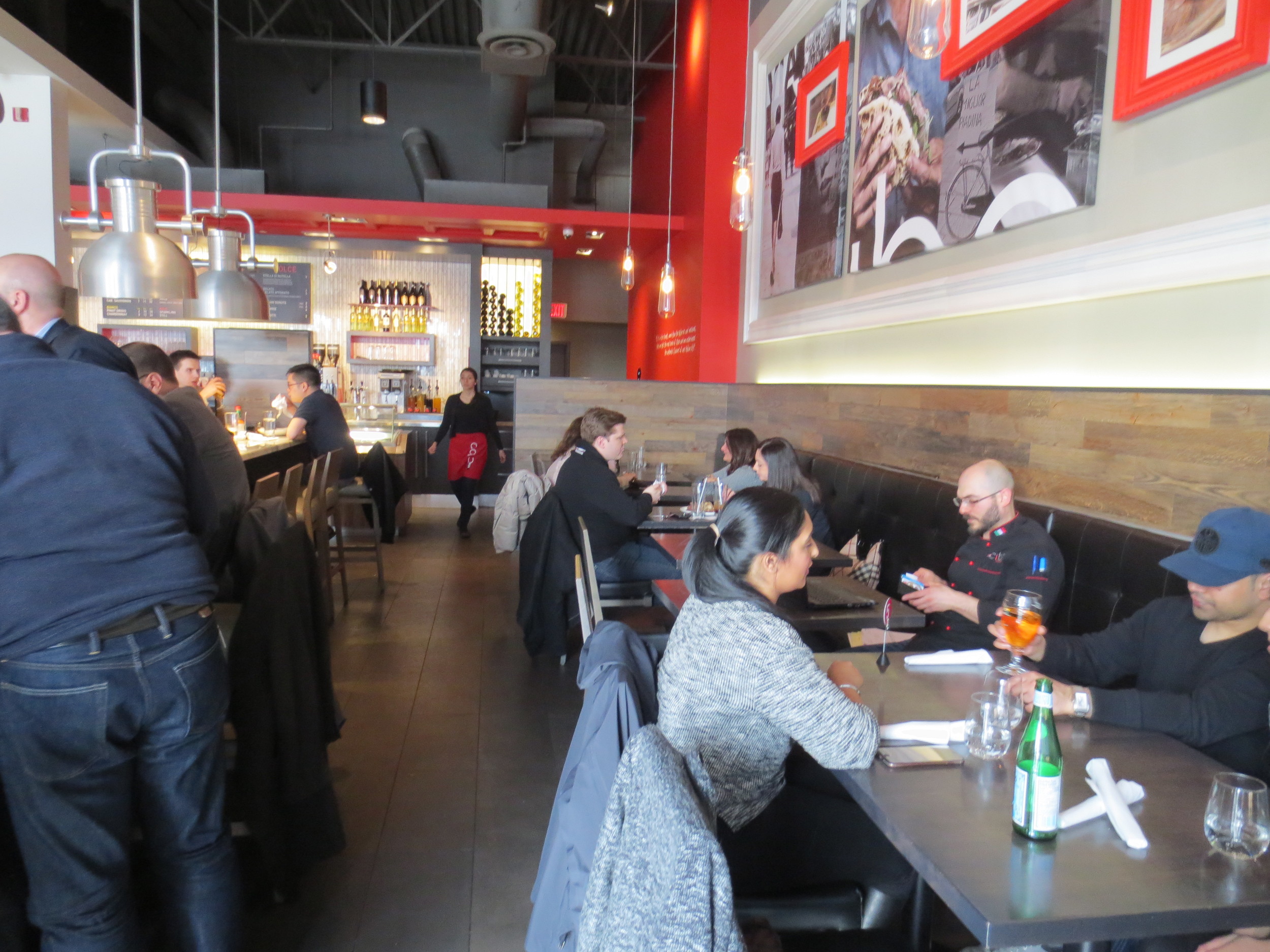 Picture of interior of restaurant. Pathway with people sitting at standard height tables.