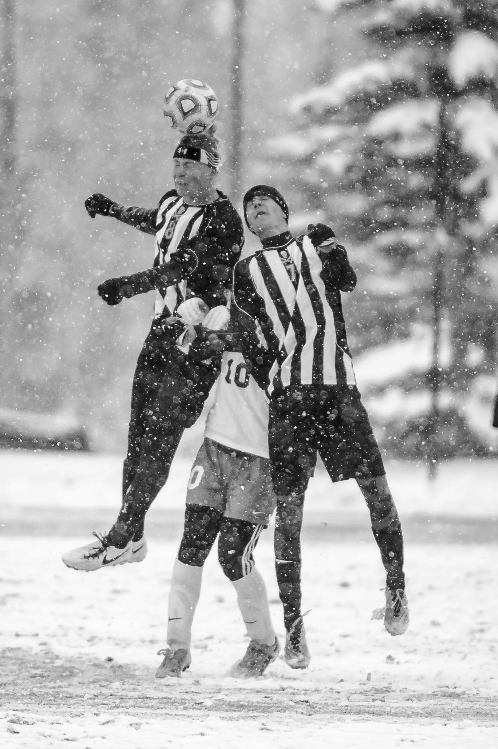Players battle for a header through a heavy snowstorm during a playoff soccer game