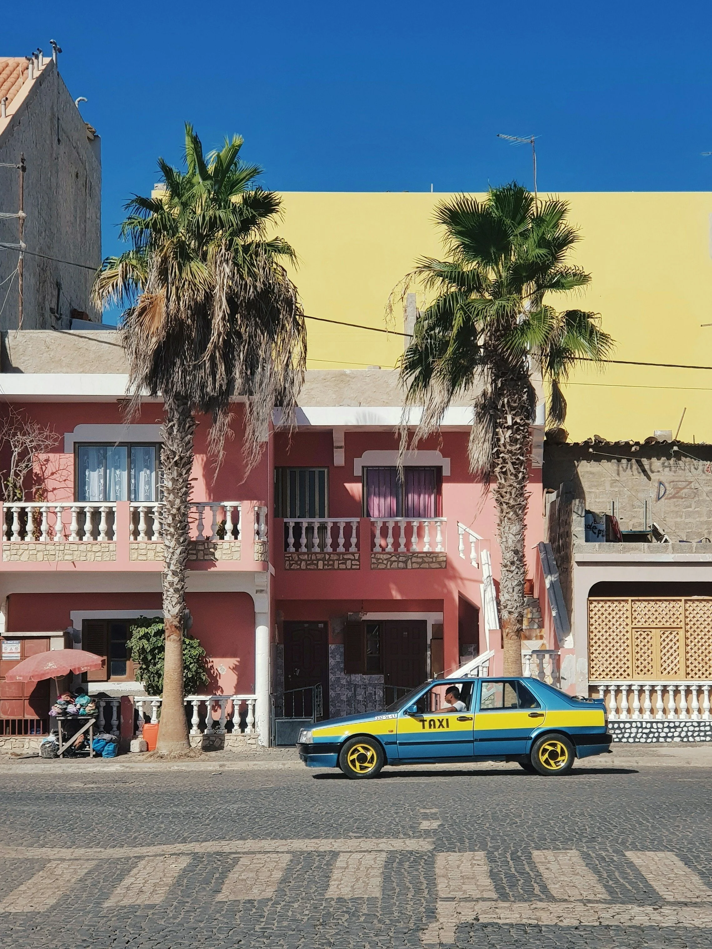 One of the famous island taxi’s in Santa Maria on Sal, Cape Verde with pink homes and palm trees in the background