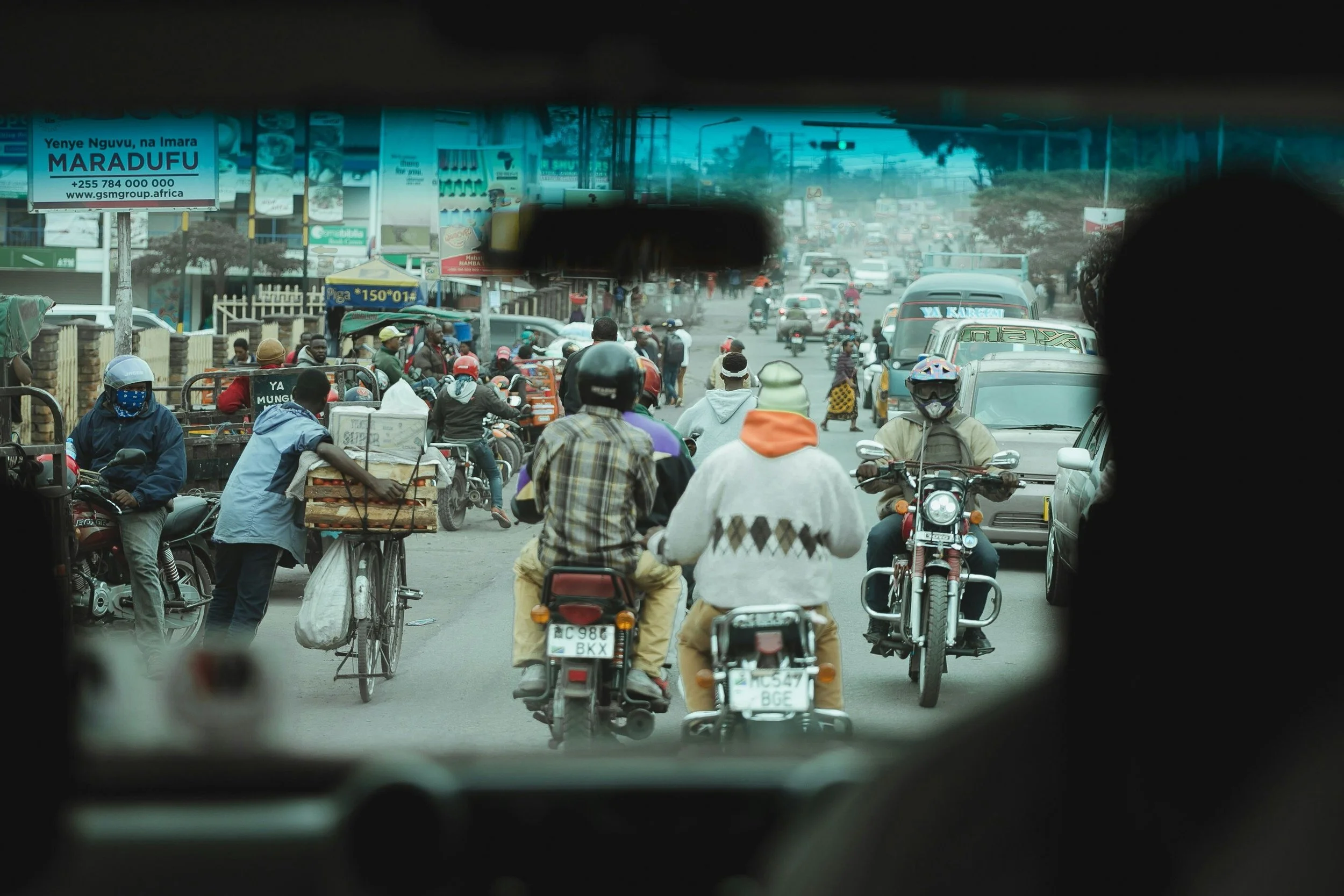 The bustling and busy town of Arusha seen through a cars front window, mopeds and bikes in its view