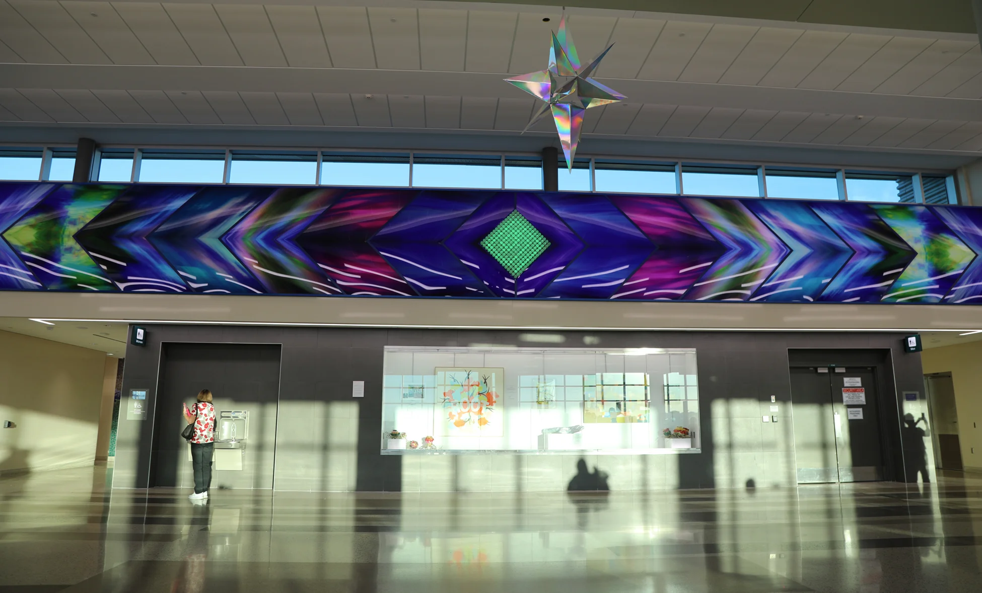Aurora Borealis, brings the colors of the Northern Lights to life in the airport. The Aurora Borealis wall is 60 feet long by 6 feet tall. In the very middle of this sixty-foot long series of images is a rainbow diamond made of clear acrylic rods and lit with LED color lights that go through the colors of the rainbow. 