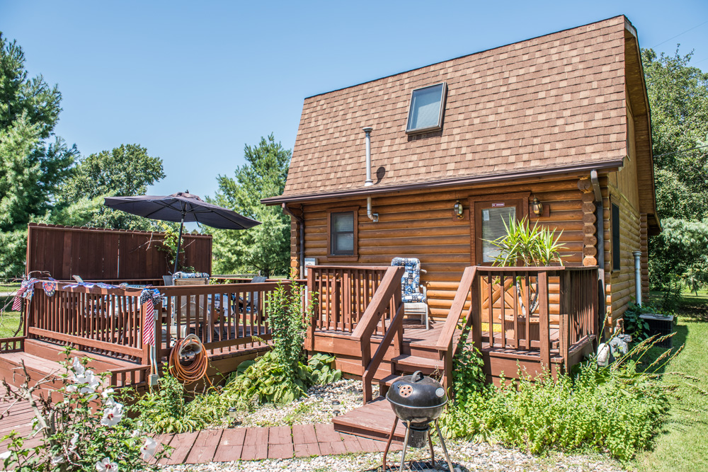  Back entrance of our authentic log cabin in Indiana with a charcoal grill in the back and a patio sitting area. 