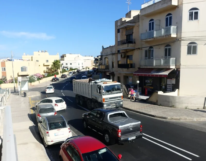 the small white car is parked in a bus zone, diagonally and with the rear sticking into the on-coming traffic. the driver is in the shop across the road.