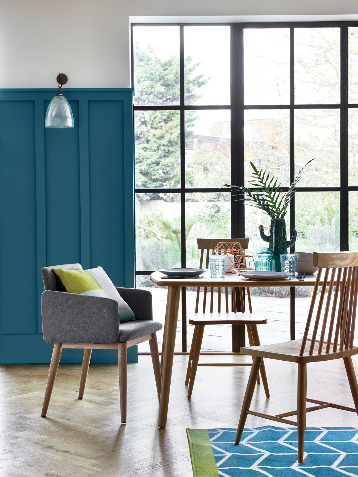 Retro upholstered grey chair, £59, Scandi Geo cushion - £6, Idris solid oak table - £259, Idris solid oak chairs - £99, Blushed pink 12 piece dinner set - £18, Jade dinner plates (set of 4) - £6, Copper wire candle holder - £10, Copper wire tealight holder - £3, Cactus vase - £12, Textured glass - £1.50, Satin Ripley 16 piece cutlery set - £15, Homemaker teal chevron rug - £40. 