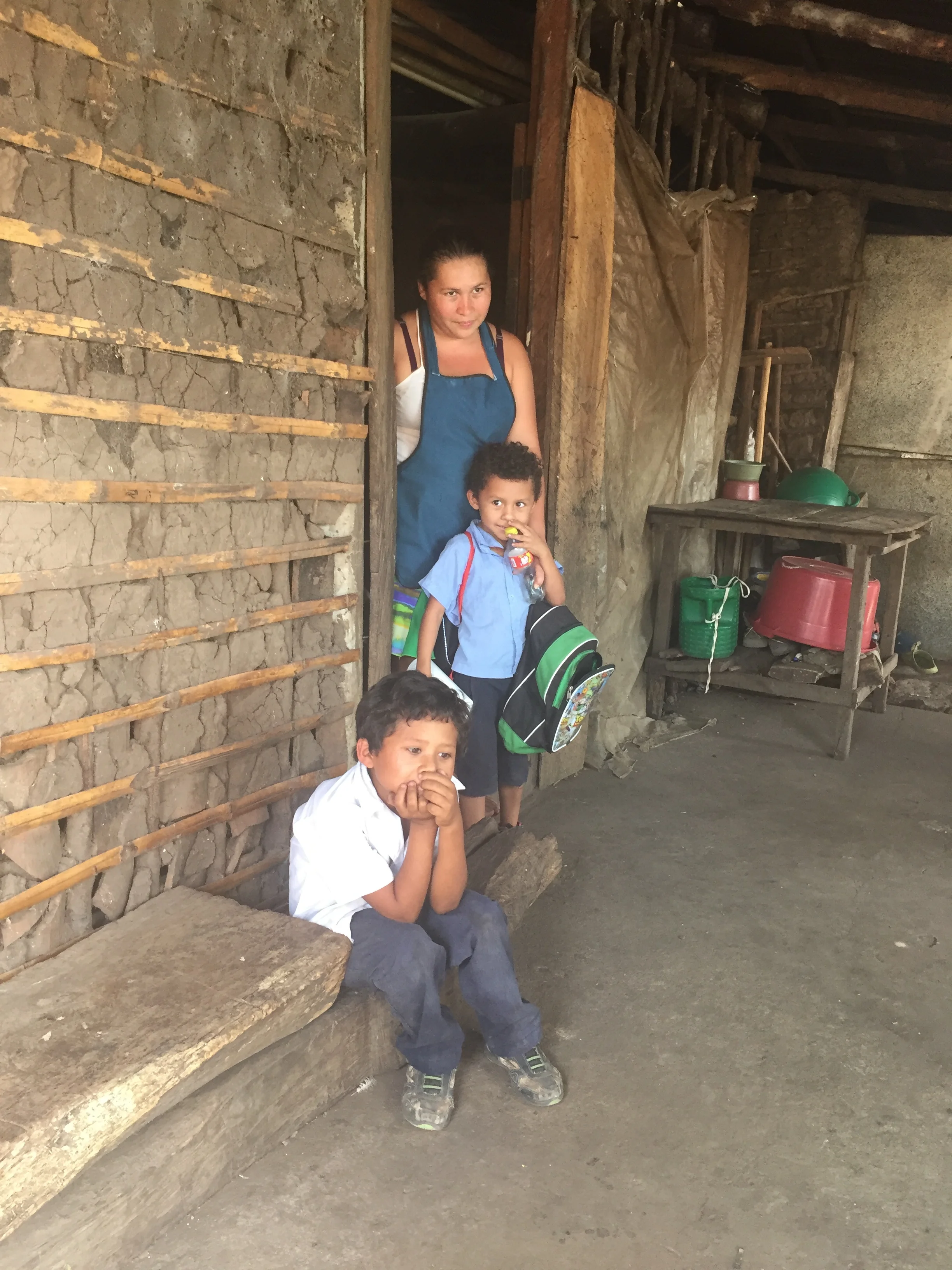 A mother with her two boys. They are in line for a toilet to be shared with her sister's family, and a home when funding comes through.