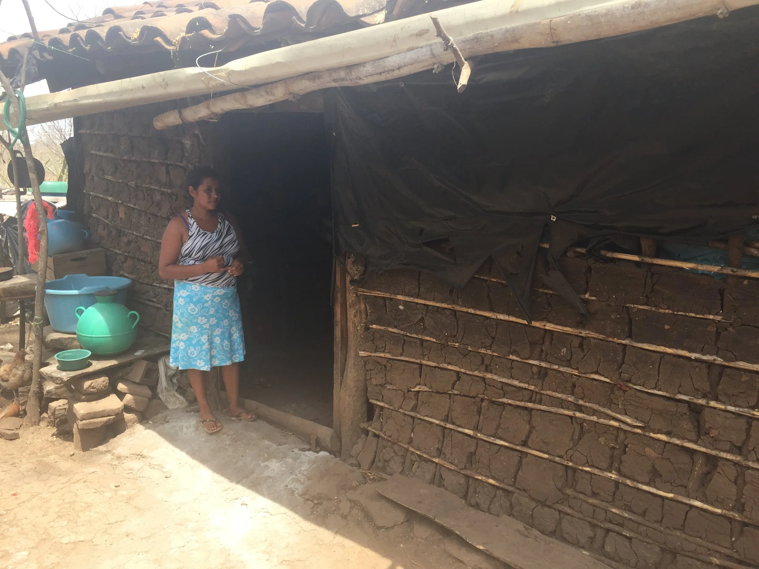 A woman waits for her children outside her home, now improved by the plastic to keep the rain out. Her water and washing containers are just behind her, ready for their next trip to the river.