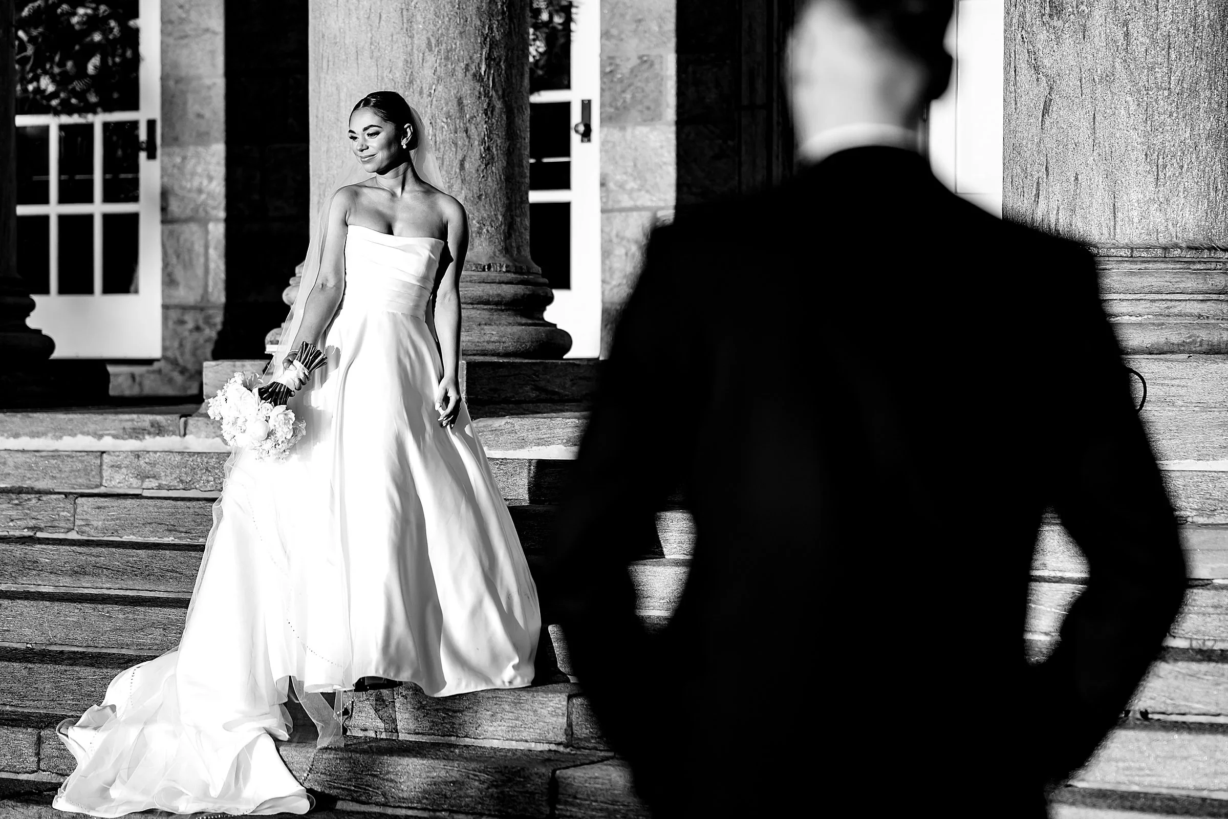 Bride on the front steps of Ballroom at Ellis Preserve, groom in the foreground