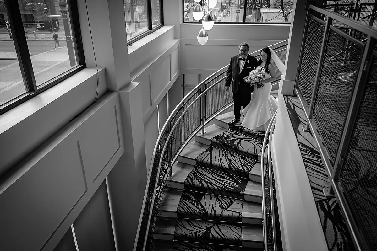 Couple walking down the curved staircase by the windows at The Lucy