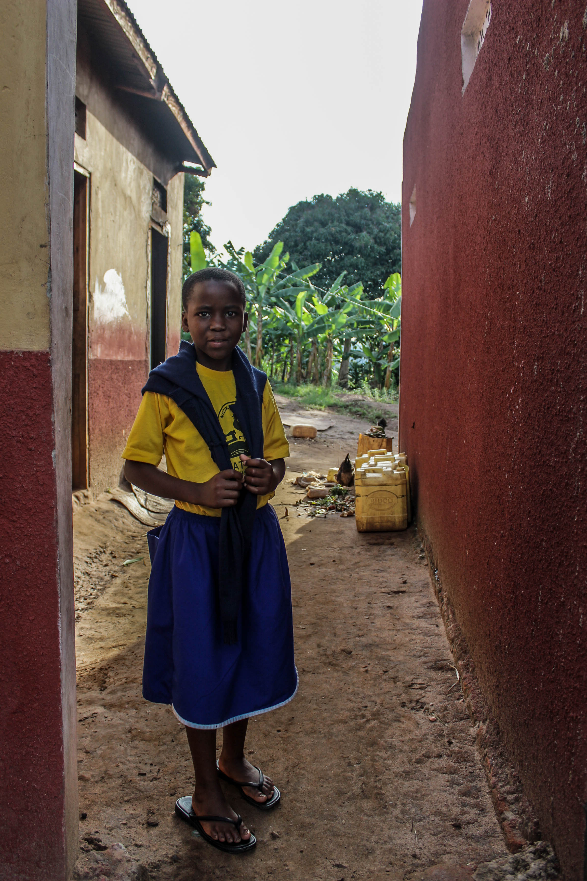 Goretti's home is a simple structure surrounded by her uncle's crops. The yellow containers behind are a constant sight in rural Uganda as they're used to carry water from a well. This can be a long journey for many children to carry many litres of water on their backs each day.