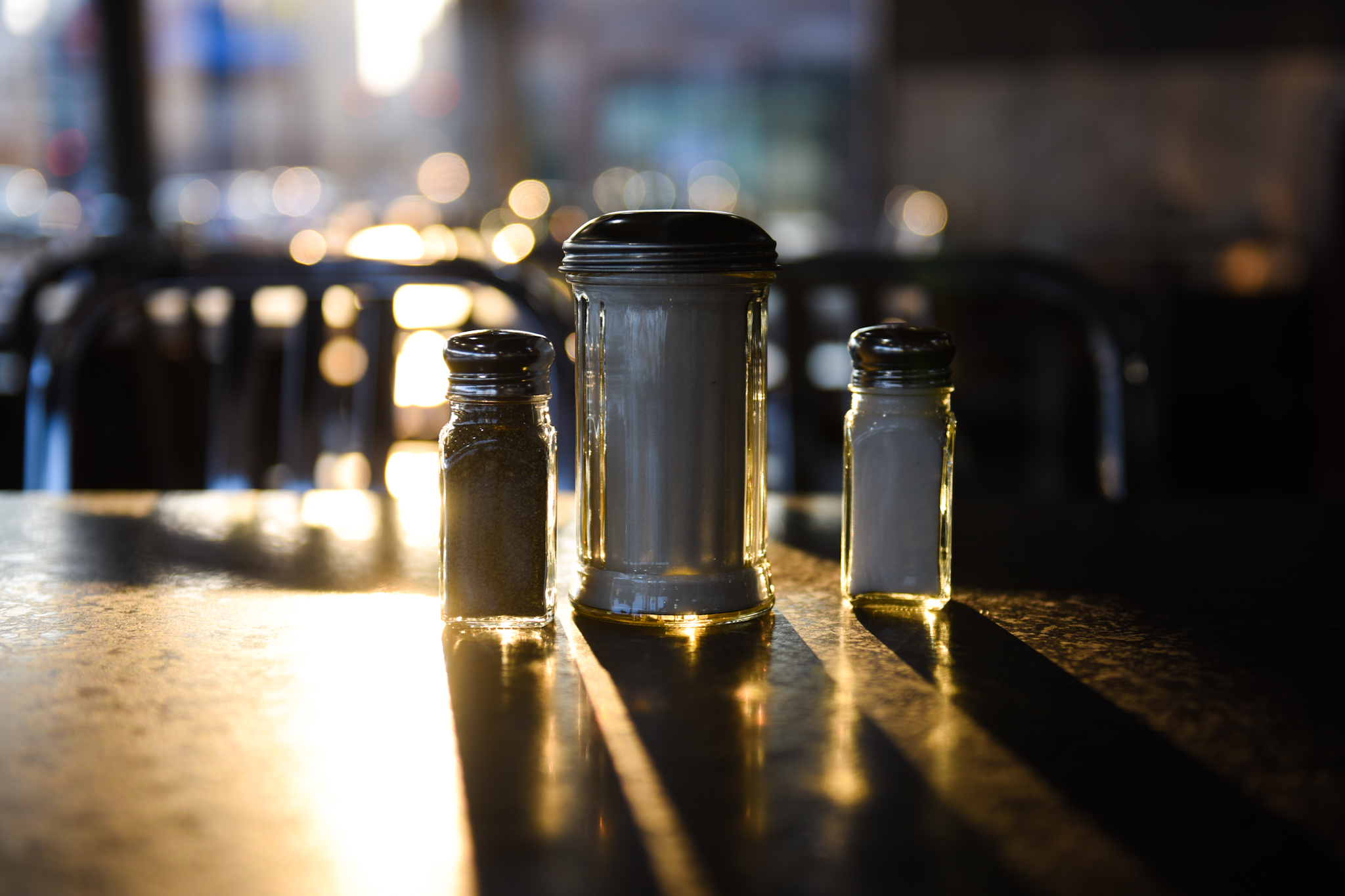 Sunlight shines through salt and pepper shakers on empty tables.
