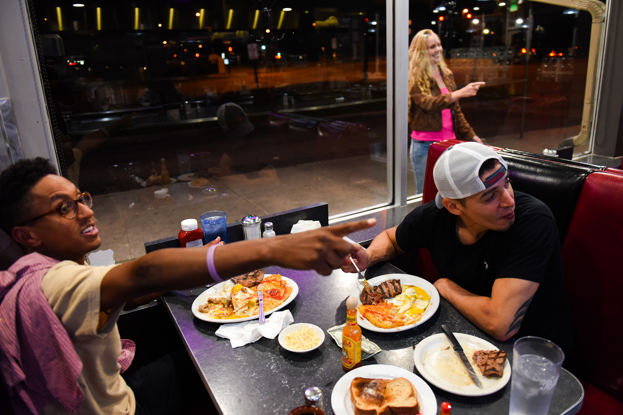 4 a.m.: Adam Tewahade (left) points as a woman smoking a cigarette tries to get her friend's attention inside the Denver Diner. Tewahade and Joe, across from him, met earlier in the night on Larimer Street.